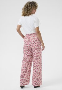 Pantalone širokog kroja s rozim leopard uzorkom, visokog struka i elastičnom trakicom. Tkanina je lagana i ima glatku teksturu.