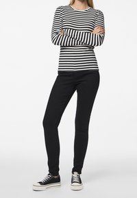 Randig långärmad skjorta i svart och vitt, i kombination med svarta slim-fit jeans och svarta sneakers med vita sulor.