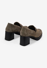 Zapatos de tacón de ante en taupe con punta redondeada y un tacón negro grueso. Presentan una textura suave y un diseño minimalista.