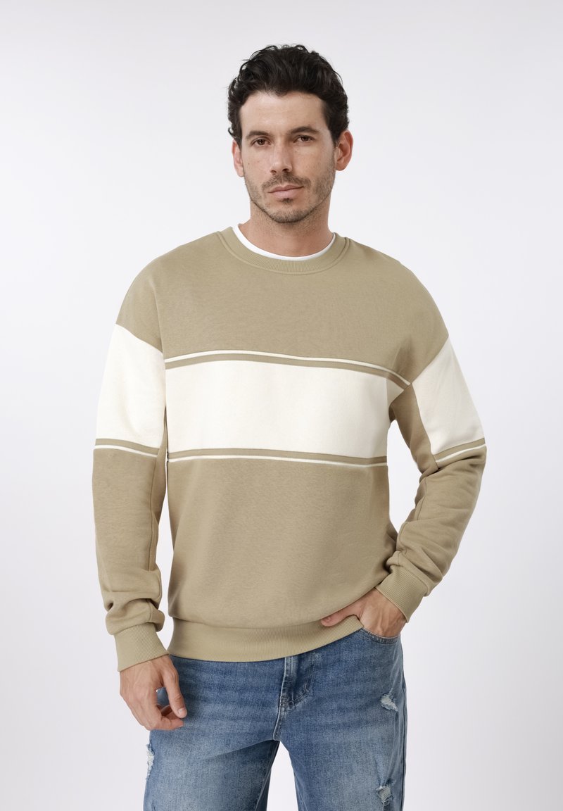 Μπεζ φούτερ με λευκές οριζόντιες ρίγες, ριμπ γιακά και μανσέτες, απαλής υφής, φορεμένο με μπλε τζιν παντελόνι με φθορές.