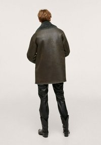 Overmaatse donkergroene jas met een getextureerde bontkraag, gecombineerd met strakke zwarte leren broeken en enkellaarsjes.