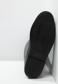 Suela de goma negra con un patrón de textura. El material superior parece ser ante con un acabado suave. Diseño de bota con una puntera redondeada.