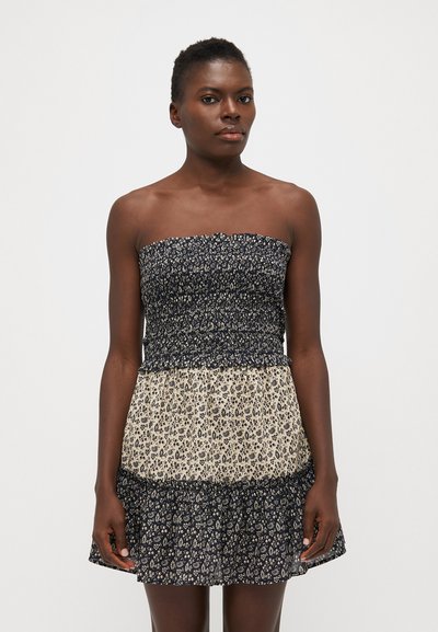 Robe sans bretelles avec un haut smocké bleu marine et une jupe beige fluide ornée d'un motif floral. Tissu doux avec un ourlet en volants à plusieurs niveaux.