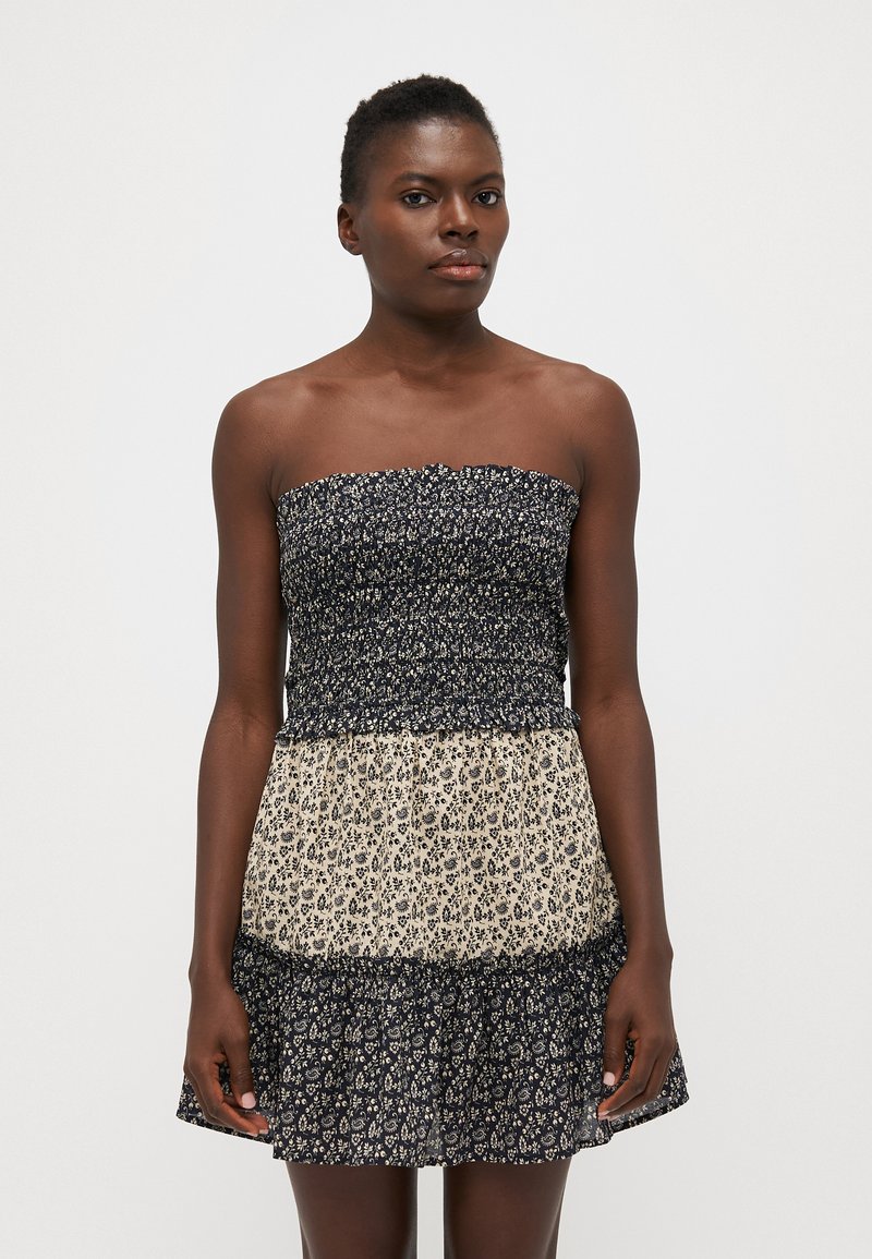 Vestido sin mangas con una parte superior de navidad fruncida en azul marino y una falda fluida beige con un patrón floral. Tela suave con un dobladillo de volantes en capas.