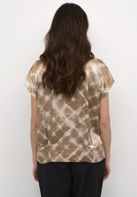 Blusa a maniche corte in un motivo tie-dye beige e marrone. Tessuto liscio e lucido con una vestibilità rilassata e sottili spacchi laterali all'orlo.