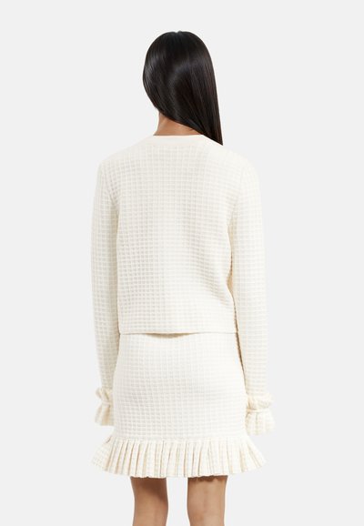 Ensemble coordonné couleur crème comprenant un pull en tricot gaufré texturé au design cropped et une mini-jupe assortie avec un ourlet festonné.