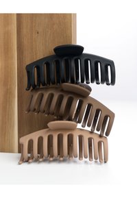 Vier Haarklammern in Schwarz, Dunkelbraun, Hellbraun und Nude. Hergestellt aus Kunststoff mit großen Zähnen und einer glatten Oberfläche. Einfaches, geschwungenes Design.