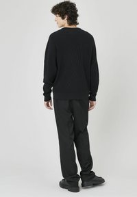Pull noir à côtes avec des manches longues, associé à un pantalon noir ample et des chaussures noires épaisses, vu de dos.