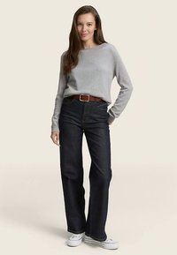 Sivi pulover z dolgimi rokavi v kombinaciji z visokim pasom temno modrih kavbojk in rjavim pasom, zaokrožen z belimi platnenimi supergami.