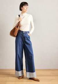 Wide-leg denim jeans with a dark blue wash and frayed light gray hems, paired with a fitted cream top and a brown suede bag.