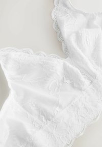 Weiße Spitzen-Bralette mit floralen Mustern und welligen Kanten, aus weichem Netzstoff mit strukturierter Oberfläche. Akzente schaffen Dimensionalität.