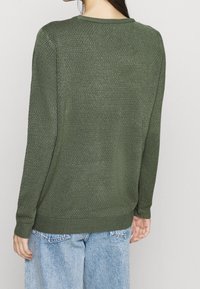 Grüner, strukturierter Pullover mit rundem Ausschnitt und gerippten Bündchen, kombiniert mit hellblauen Denim-Jeans. Die Rückansicht zeigt eine lockere Passform und einfarbige Farbe.