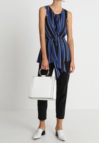 Mörkblå och svarta randiga ärmlösa top med knyt i midjan, ihop med svarta jeans, vita klackar och en vit väska med guld detaljer.