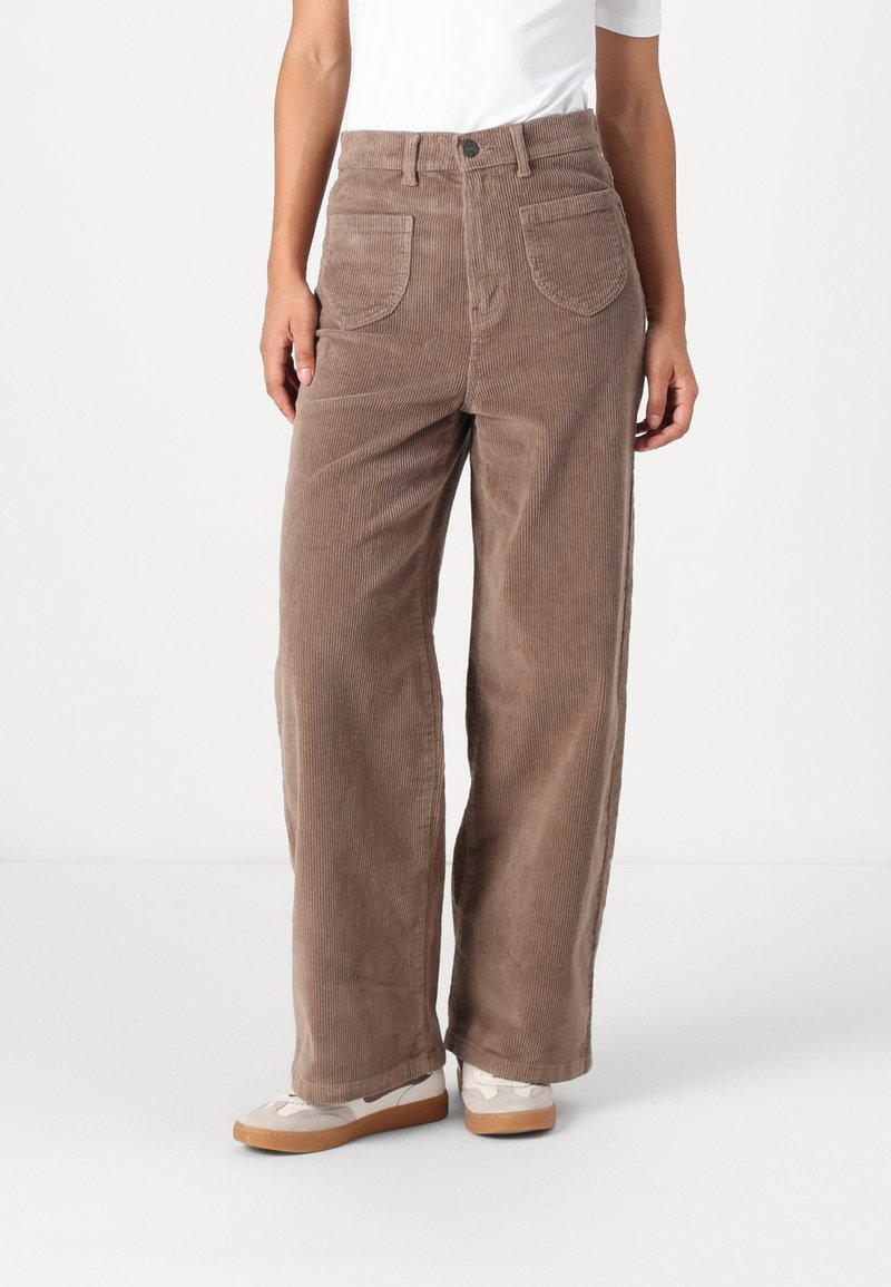 Bruine corduroy wijde broek met twee voorzakken, textiele stof, hoge taille en een knoopsluiting. Draagt met casual schoenen.