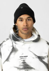 Zwart gebreid beanie, geribbelde textuur, goed aansluitend bovenaan. Witte hoodie met abstracte grijze patronen en bedrukt tekst, verstelbare trekkoord bij de hals.