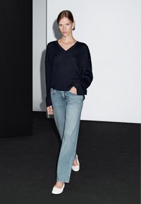 Marinblå stickad tröja med V-ringning, ihop med ljusblå raka jeans och vita lägenheter. Outfiten har en avslappnad passform och ribbad textur.