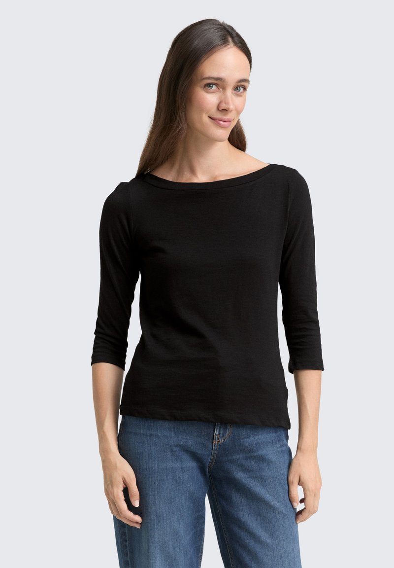 Schwarzes Langarm-T-Shirt mit weitem Ausschnitt, aus weichem, glattem Stoff gefertigt. Kombiniert mit blauen Jeans, die einen lässigen Schnitt und Stil zeigen.