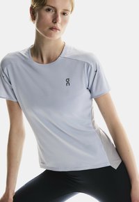 Hellblaues Sportshirt mit kurzen Ärmeln, rundem Halsausschnitt, atmungsaktivem Material und schwarzem Logoakzent auf der linken Brust.