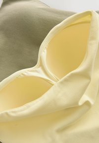 Soutien-gorge rembourré en tissu côtelé doux jaune pastel et vert olive, montrant les détails des bonnets et des bretelles.