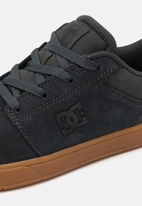Dark gray suede sneaker featuring a black logo, textile accents, flat black laces, and a brown rubber outsole.