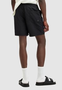 Shorts neri in nylon con cinturino elastico, tasca piatta sul retro e occhielli. Abbinati a sandali neri e calzini bianchi a coste.