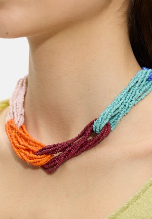Wielokolorowy naszyjnik z koralików z nitkami w kolorach turkusowym, burgundowym, pomarańczowym i różowym, noszony na szyi osoby na jasnym tle.