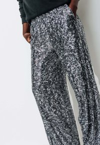 Pantalons fluides en sequins noirs et argentés avec taille élastique, présentant une texture côtelée et des poches latérales, assortis à un haut noir.