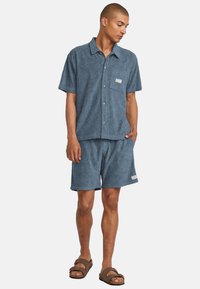 Camisa de manga corta azul y pantalones cortos a juego con un patrón floral texturizado. La camisa cuenta con un bolsillo en el frente; los pantalones cortos tienen un bolsillo lateral.