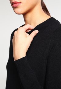 Maglione nero realizzato in materiale morbido, con un colletto a coste e maniche lunghe, dalla forma aderente messa in risalto da una mano vicino al colletto.