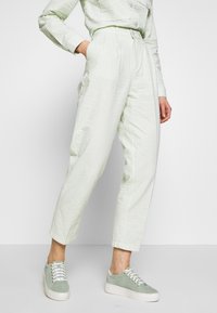 Light green patterned pants with a textured finish, high waist, and front pleats, paired with light green sneakers and a matching shirt.