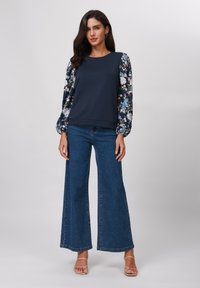 Marineblå topp med blomster, puffermarmer; denim flared bukser; lett tekstur; uformelt antrekk ideelt for avslappede settinger.