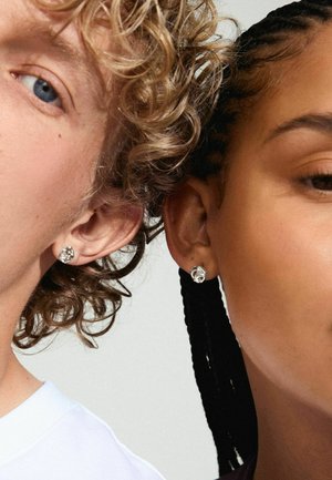 Silver stud earrings with a floral design, featuring textured details. The wearers have different hairstyles and skin tones.