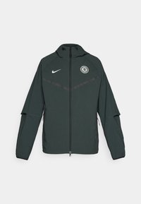 Dark green Nike jacket with a hood, front zipper, Chelsea FC logo on the left chest, and contrasting black horizontal stripes.