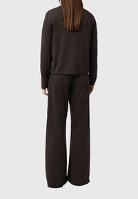 Ciemnobrązowy dziergany sweter z krótkim dołem, zestawiony z szerokimi brązowymi spodniami, oba elementy cechuje minimalistyczny design i miękka struktura.