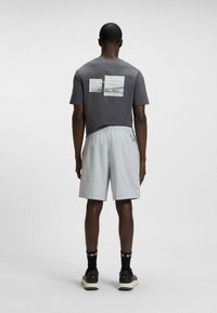 Grijze t-shirt met twee fotografische afdrukken op de achterkant, gecombineerd met lichtgrijze shorts. Beide kledingstukken zijn gemaakt van ademende stof.