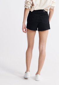 Black denim shorts with a frayed hem, high waist, and two back pockets; paired with a light beige oversized top and white sneakers.
