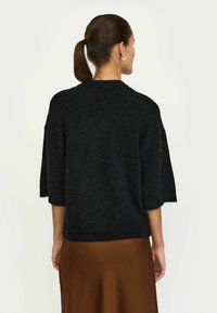 Melna pārspīlēta džemperis ar īsām piedurknēm, izgatavots no mīksta materiāla. Ievērojama tekstūra un brīvs piegriezums. Apvienots ar brūnu svārku.