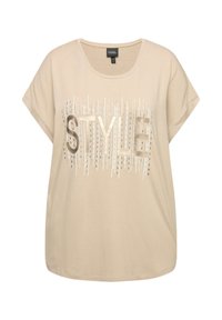 Krémové tričko s krátkým rukávem vyrobené z měkké látky, ozdobené nápisem "STYLE" v metalickém písmu s vertikálními liniemi. Oblé výstřih.