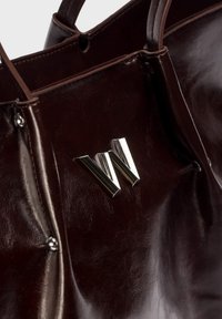 Bruine lederen tote bag met een glanzende afwerking, voorzien van een metallic zilveren 'W' logo en decoratieve hardwareaccenten.