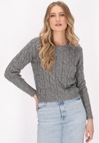 Grauer Kabelstrickpullover mit langen Ärmeln und rundem Ausschnitt, kombiniert mit einem hellblauen Jeansrock. Strukturmuster über das gesamte Teil.