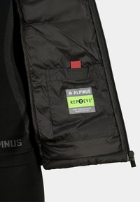 Czarna ocieplana kamizelka z zamkiem, z zieloną metką Repreve, czerwonym akcentem i wewnętrzną kieszenią. Wykonana z recyklingowanych butelek plastikowych.