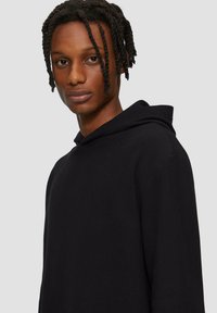 Zwarte geribde hoodie met een trekkoord, voorzien van een relaxed fit en een gestructureerde stof. Geen zichtbare patronen of logo's. Eenvoudig ontwerp.