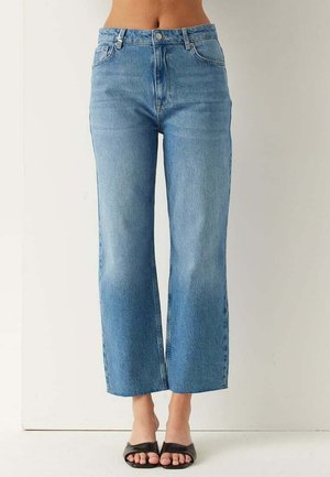 Jeans azzurri a vita alta e gamba dritta, abbinati a sandali neri aperti senza cinturini, su sfondo bianco neutro.