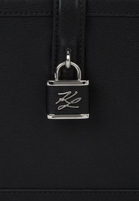 Czarna skórzana torebka z srebrnym zamkiem z grawerowanym logo, o gładkiej fakturze i prostych liniach, zaprojektowana z myślą o minimalistycznym wyglądzie.