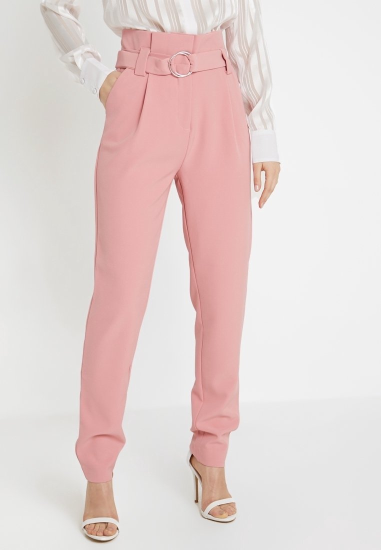 Pantalon rose taille haute avec ceinture et boucle circulaire argentée, associé à un chemisier rayé et des sandales blanches à talons hauts.