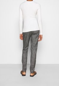 Weißes, geripptes Langarmoberteil kombiniert mit grauen gemusterten Hosen, die einen schlanken Schnitt haben, sowie Sandalen mit flachem Absatz. Rückansicht des Outfits.