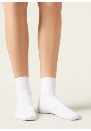 Weiße Knöchelsocken aus geripptem Baumwollmischgewebe mit weicher Textur und elastischem Bund, gezeigt an bloßen Beinen vor einem neutralen Hintergrund.
