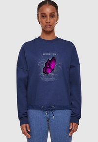 Felpa blu navy con grafica di una farfalla in viola e testo bianco. Presenta un orlo con coulisse e polsini a coste. Materiale in cotone morbido.
