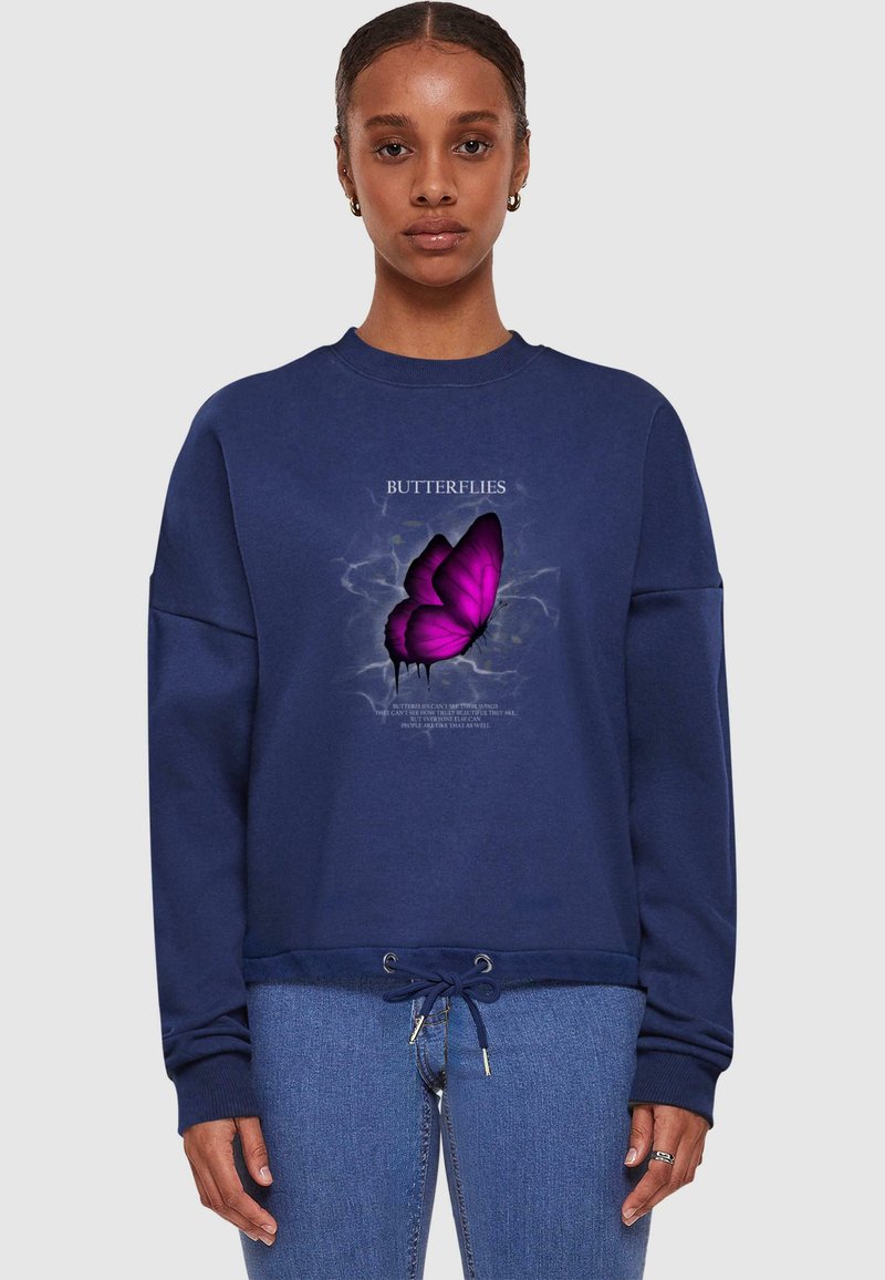 Granatowy sweatshirt z grafiką motyla w fioletowym i białym kolorze. Posiada ściągacz na dole oraz prążkowane mankiety. Wykonany z miękkiego materiału bawełnianego.