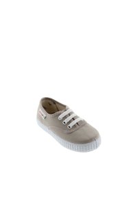 Zapatillas de lona beige con cordones blancos, suela de goma y puntera redondeada. Presenta una etiqueta con el logotipo en el lateral y un detalle de costura en contraste.